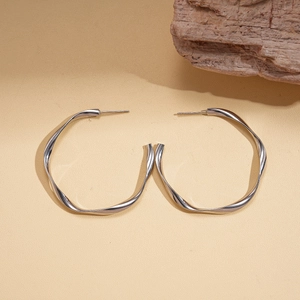 Silver geometric twisted hoop earrings with a polished finish on textured leather surface