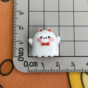White cartoon ghost resin charm with red bow measured on a scale for size reference