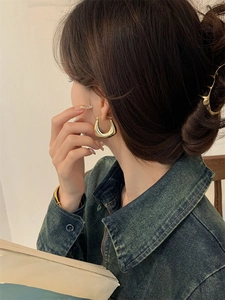 Gros plan d'une boucle d'oreille dorée en forme de U portée par un mannequin élégant