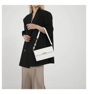 Close-up of a white vintage crossbody bag with gold buckle and chain strap on a model