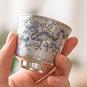 Taza de té de plata con patrón de dragón azul y sello 999 sostenida en mano