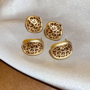 Detail of leopard print geometric earrings on silk background with gold metal finish