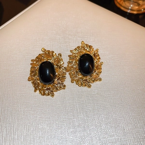 Macro detail of French vintage gold leaf earrings with oval black stones and relief texture