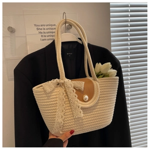 Detail of straw tote bag featuring a pearl buckle closure and elegant lace ribbon bow