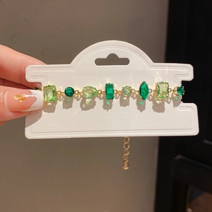 Close-up of gold chain bracelet with multi-shape green gemstones on a jewelry card
