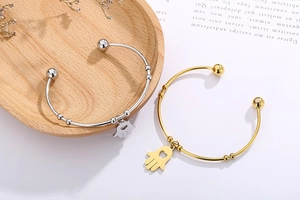 Close-up of gold and silver Hamsa Hand open bangles with hollow heart charms on wood