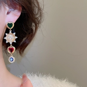 Detail view of long vintage drop earring with green and red zircon hearts and evil eye charms