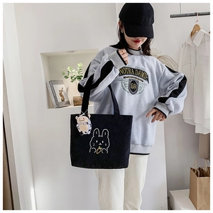 Detail of black corduroy tote bag with cute rabbit embroidery and cow plush charm