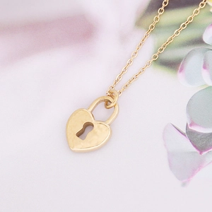 Dettaglio di una collana con ciondolo a lucchetto a cuore dorato su sfondo floreale