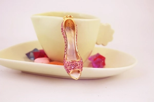 Pink rhinestone high heel keychain with gold metal clasp hanging on a ceramic cup