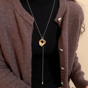 Detail einer minimalistischen Goldkette mit unregelmäßigem Kreisanhänger über einem Pullover