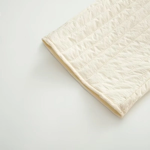 Close-up of quilted wave pattern and hemmed edge texture on cream white fabric