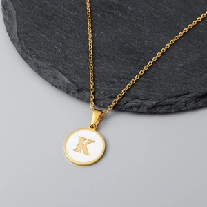 Detailed view of an 18K gold letter K shell pendant on a textured black stone