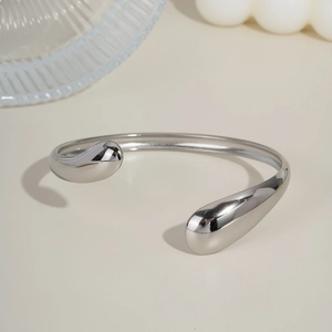 Close-up of polished silver teardrop open bangle on a minimalist white aesthetic setup