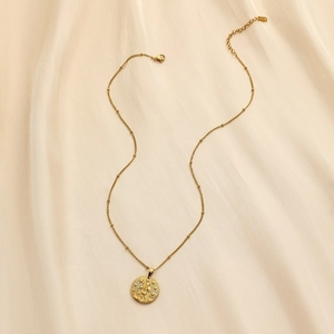 Detail of a gold stainless steel coin necklace with zodiac embossing on beige silk fabric