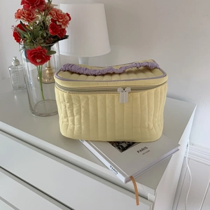 Detailed side view of yellow quilted velvet makeup bag with purple handles in a home setting