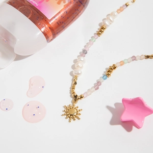Close-up of golden sun pendant necklace with fresh pearls and colorful stones on white background