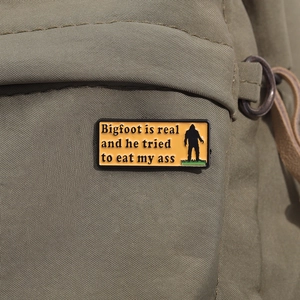 Macro view of funny Bigfoot enamel pin on green canvas bag showing humor design