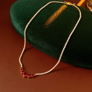 Close-up of a gold necklace with five graduated red gemstones on green velvet display