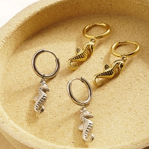 Detailed view of gold and silver seahorse hoop earrings on a beige textured tray