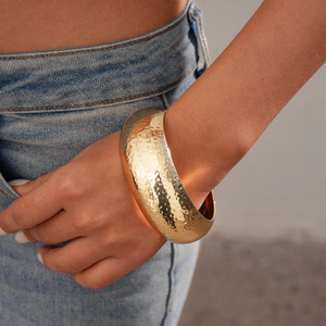 Detail of wide golden cuff bracelet with hammered texture worn on a female wrist