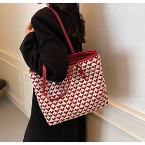 Detailed side view of large tote bag featuring red heart patterns and leather handles