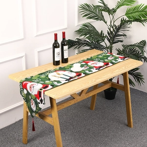 Close-up of green Christmas table runner with Santa motifs and red tassels on wooden table