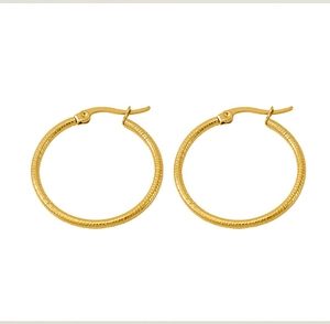 Macro detail of golden titanium steel hoop earrings with delicate spiral textured pattern