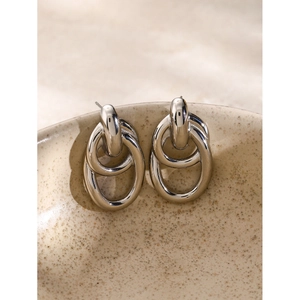 Macro detail of polished silver intertwined hollow earrings on a ceramic bowl