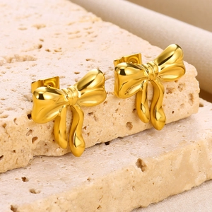 Macro shot of 18K gold plated stainless steel bow earrings on a textured stone surface