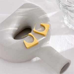 Minimalist matte gold square hoop earrings displayed on elegant white ceramic pottery