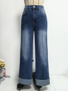 Detail van wijde blauwe jeans met middennaad aan de voorkant en gewassen denimtextuur