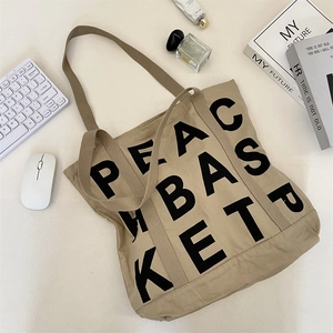 Detail of khaki canvas tote with black PEAC BASKET print on a minimalist white desk