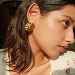 Elegant gold shell earrings in stainless steel worn by a model in warm sunlight
