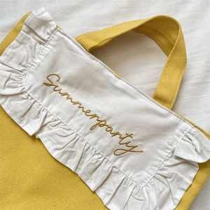 Detail of yellow canvas tote with white ruffles and Summerparty golden embroidery