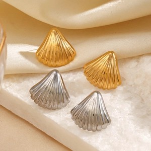 Chic gold and silver shell earrings displayed on a white stone with silk background