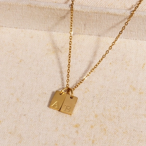 Close-up of gold-plated square letter pendants A and B on stainless steel chains