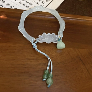 Gros plan d'un bracelet en jade forme bambou avec ornement lotus et pendentif gland