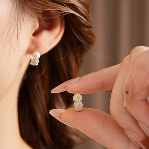 Macro detail of vintage daisy enamel hoop earrings featuring white and yellow flower petals
