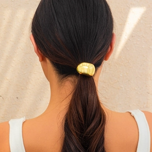 Close-up of a minimalist gold metal hair tie with irregular geometric surface for women