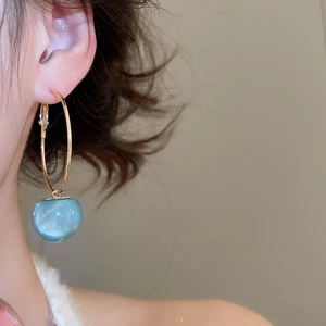Close-up of minimalist gold hoop earring with light blue resin ball pendant on model ear
