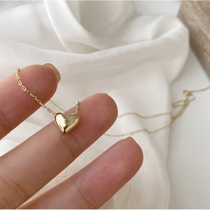 Close-up of polished 18K gold heart pendant necklace held between fingers for detail