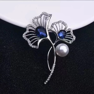 Elegant silver flower brooch with blue gemstones and white pearl on dark textured background