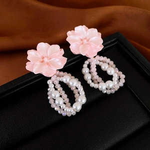 Détail de boucle d'oreille fleur rose avec perles et cristaux sur fond en soie brune