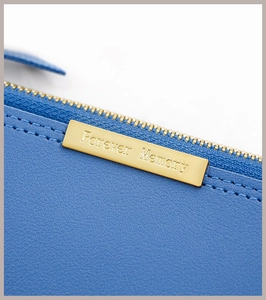 Gros plan sur la fermeture dorée et plaque Forever Memory sur portefeuille en cuir bleu