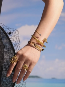 Close-up of 18K gold plated sun rings and zircon bangles against a sunny beach sky