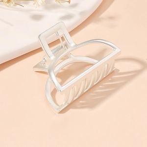 Macro view of a silver metal arch-shaped hair claw clip on a soft pink desk