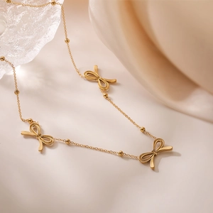 Elegant gold bow pendant necklace with small beads displayed on soft beige silk background
