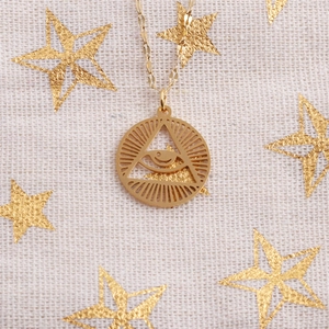 Close-up of a gold-toned stainless steel evil eye pendant necklace on a star-patterned background