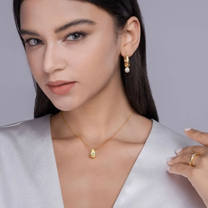 Detail of elegant gold pear-cut moissanite necklace, earrings, and ring set on a model